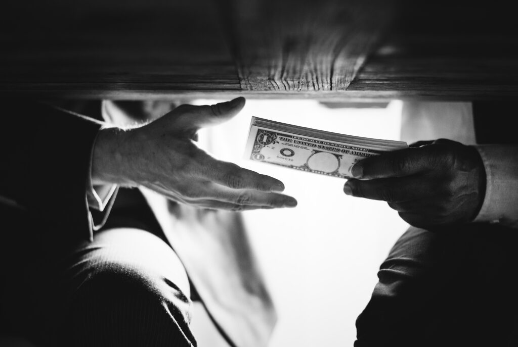 hands passing money under table corruption bribery
